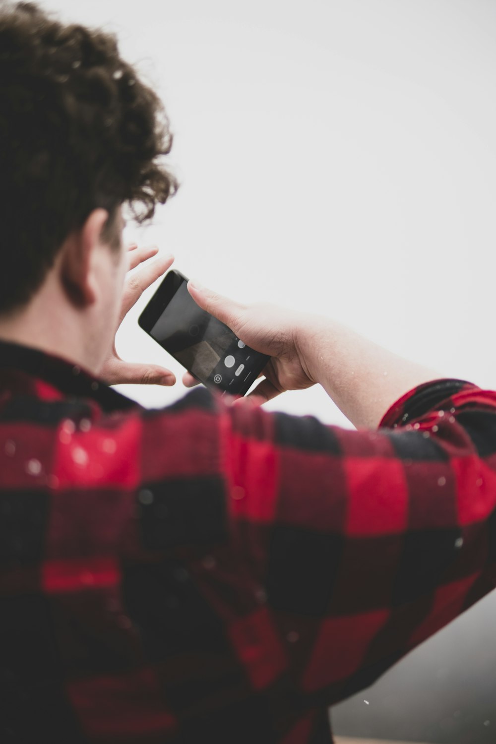 man in red and white checked shirt holding black smartphone
