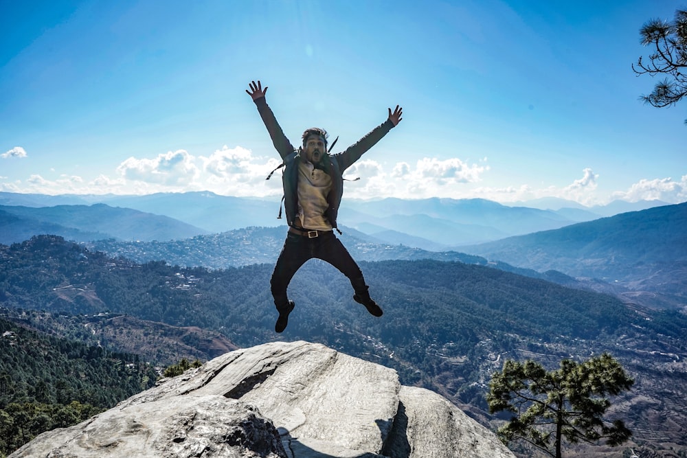 man in brown jacket jumping on mountain during daytime