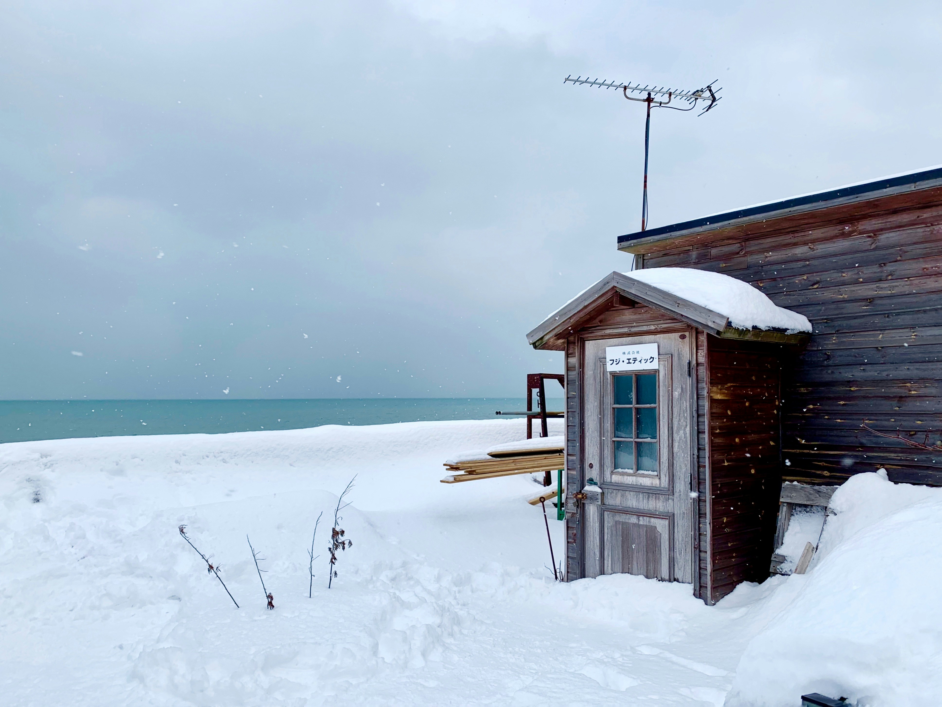 casa di legno marrone su terreno coperto di neve vicino allo specchio d'acqua durante il giorno