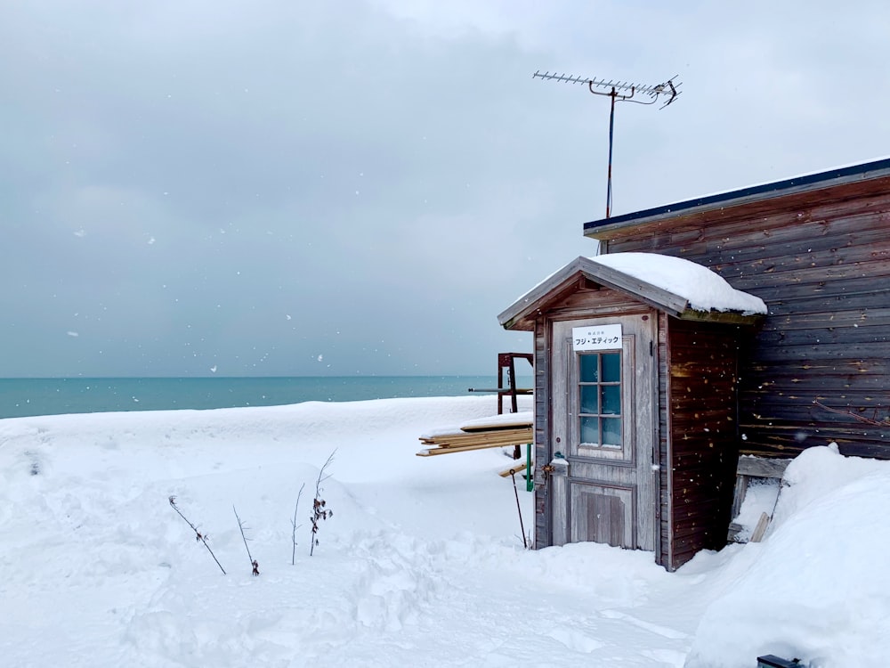 Casa de madera marrón en un terreno cubierto de nieve cerca del cuerpo de agua durante el día