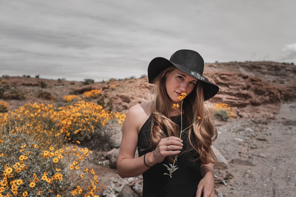 woman in black tank top and black hat standing on yellow flower field during daytime