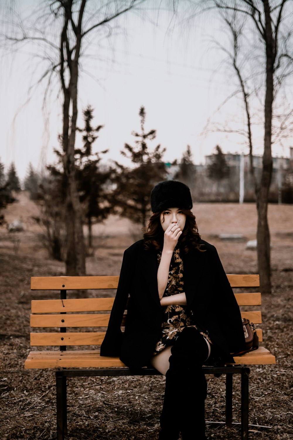 woman in black coat sitting on brown wooden bench during daytime