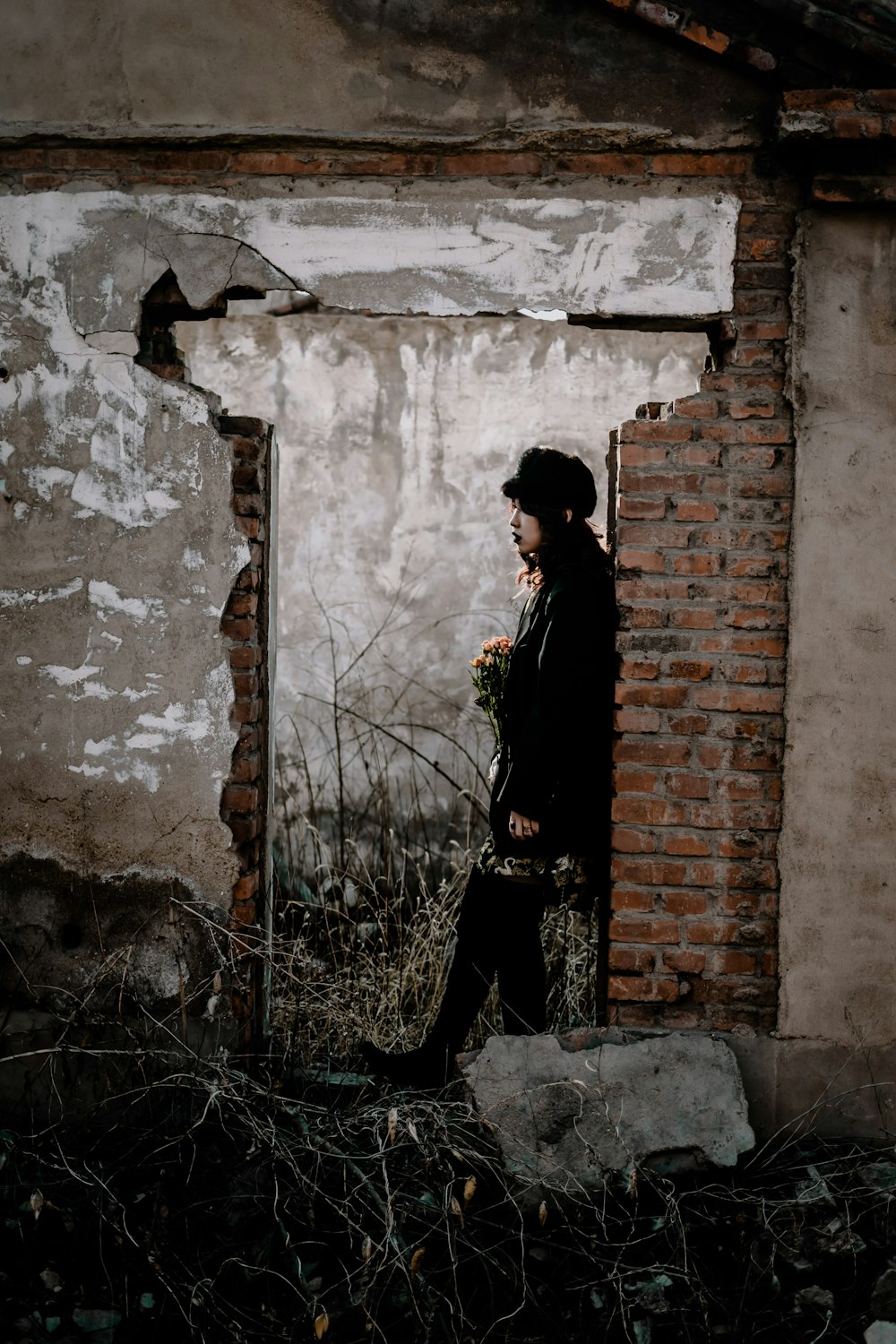 uomo in cappotto nero in piedi accanto al muro di mattoni marroni durante il giorno