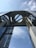An imposing architectural structure with a modern design, featuring a large circular opening at the top surrounded by glass and metal elements. The perspective looks upward towards a blue sky with wispy clouds.