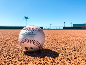 white and red baseball on brown soil during daytime