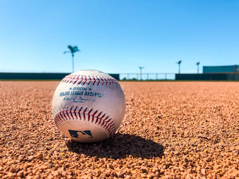 white and red baseball on brown soil during daytime