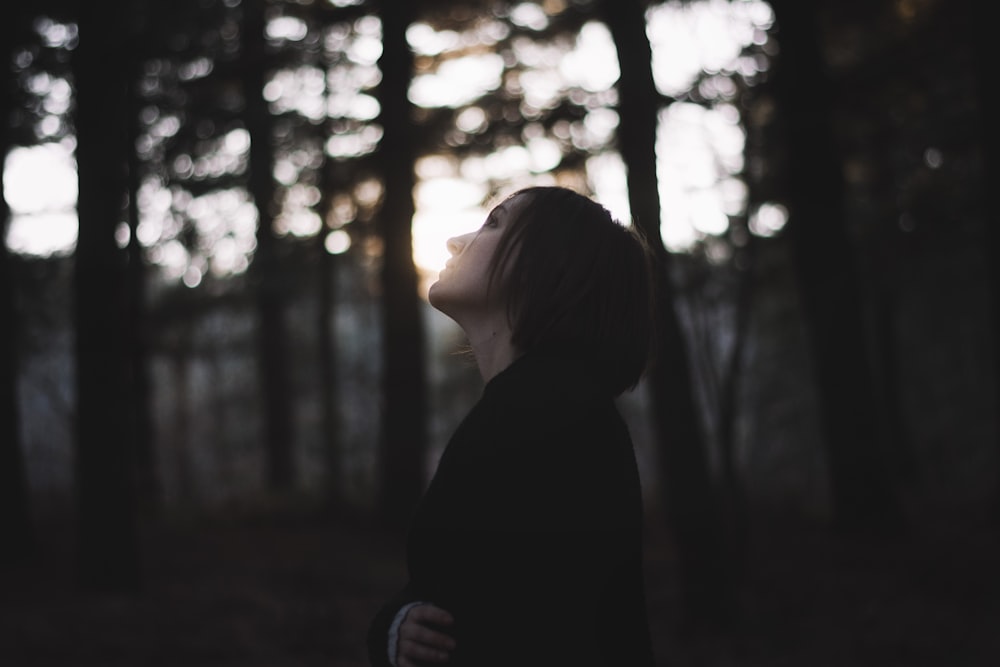 femme en manteau noir debout devant les arbres pendant la journée