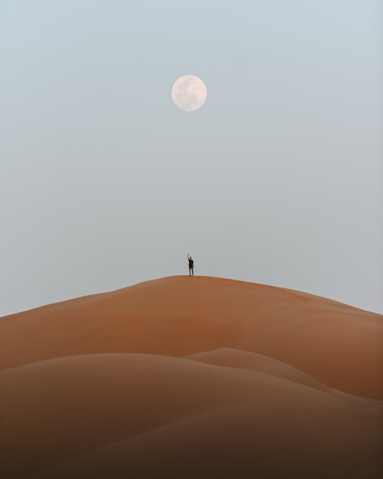 man standing on desert under full moon in Abu Dhabi United Arab Emirates