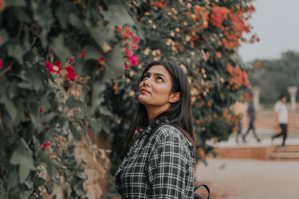 woman in black and white plaid dress shirt standing near red flowers during daytime