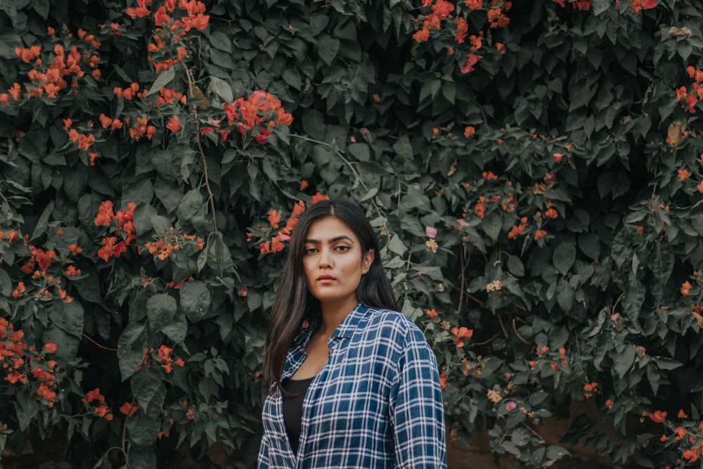 woman in blue and white plaid dress shirt standing beside red flowers