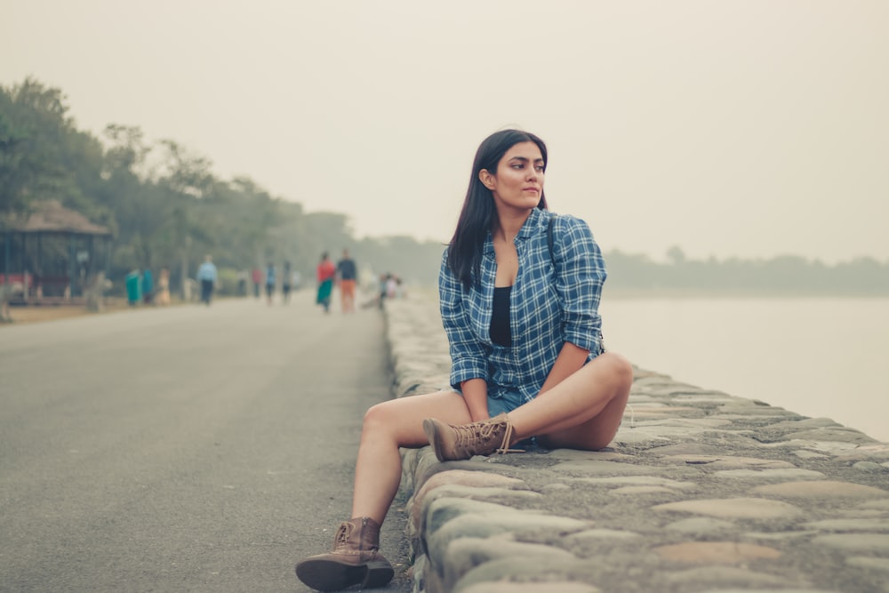 woman in blue and white plaid dress shirt and brown pants sitting on brown rock during