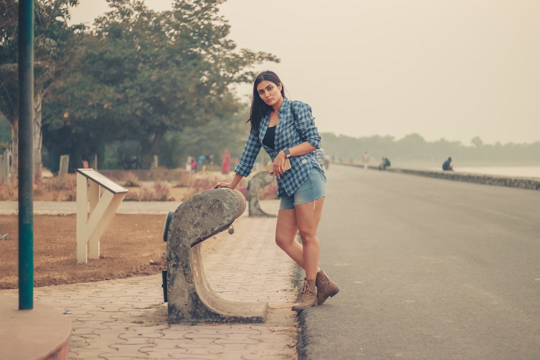 woman in blue and white plaid dress shirt and blue denim shorts standing on brown concrete
