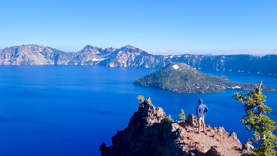 2 person standing on brown rock formation near blue lake during daytime