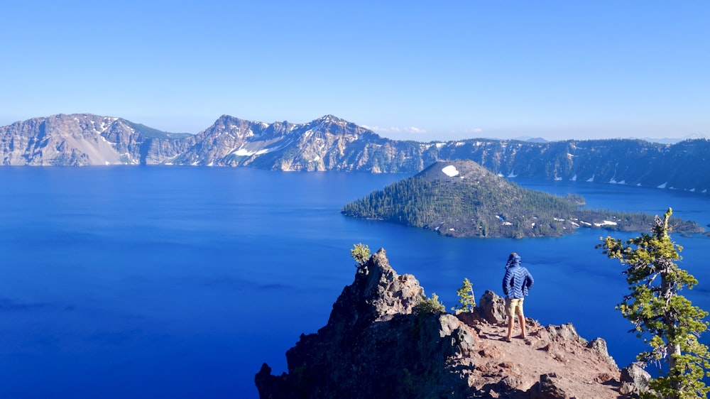 2 person standing on brown rock formation near blue lake during daytime