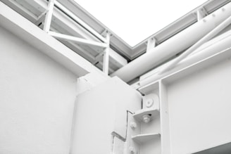 A close-up view of a white architectural structure with exposed beams and joints. The image features clean lines and geometric shapes, showcasing the technical design of the building.