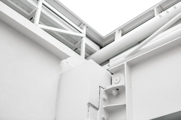 A close-up view of a white architectural structure with exposed beams and joints. The image features clean lines and geometric shapes, showcasing the technical design of the building.