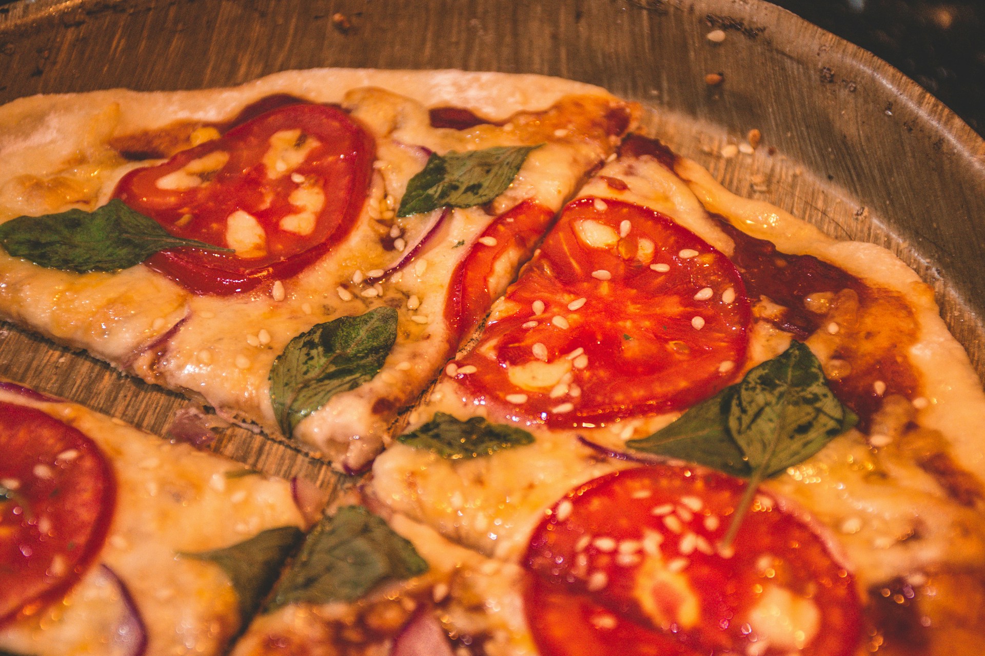 Close-up of a freshly baked thin-crust pizza topped with vibrant tomatoes, basil, and melted mozzarella cheese on a rustic wooden table.