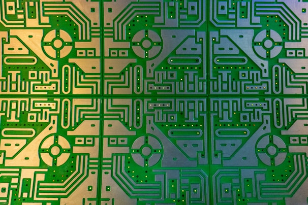 Complex and detailed circuit board featuring symmetrical patterns and intricate pathways. The design includes a repeating geometrical motif with rounded and linear elements, embedded with multiple holes for components.