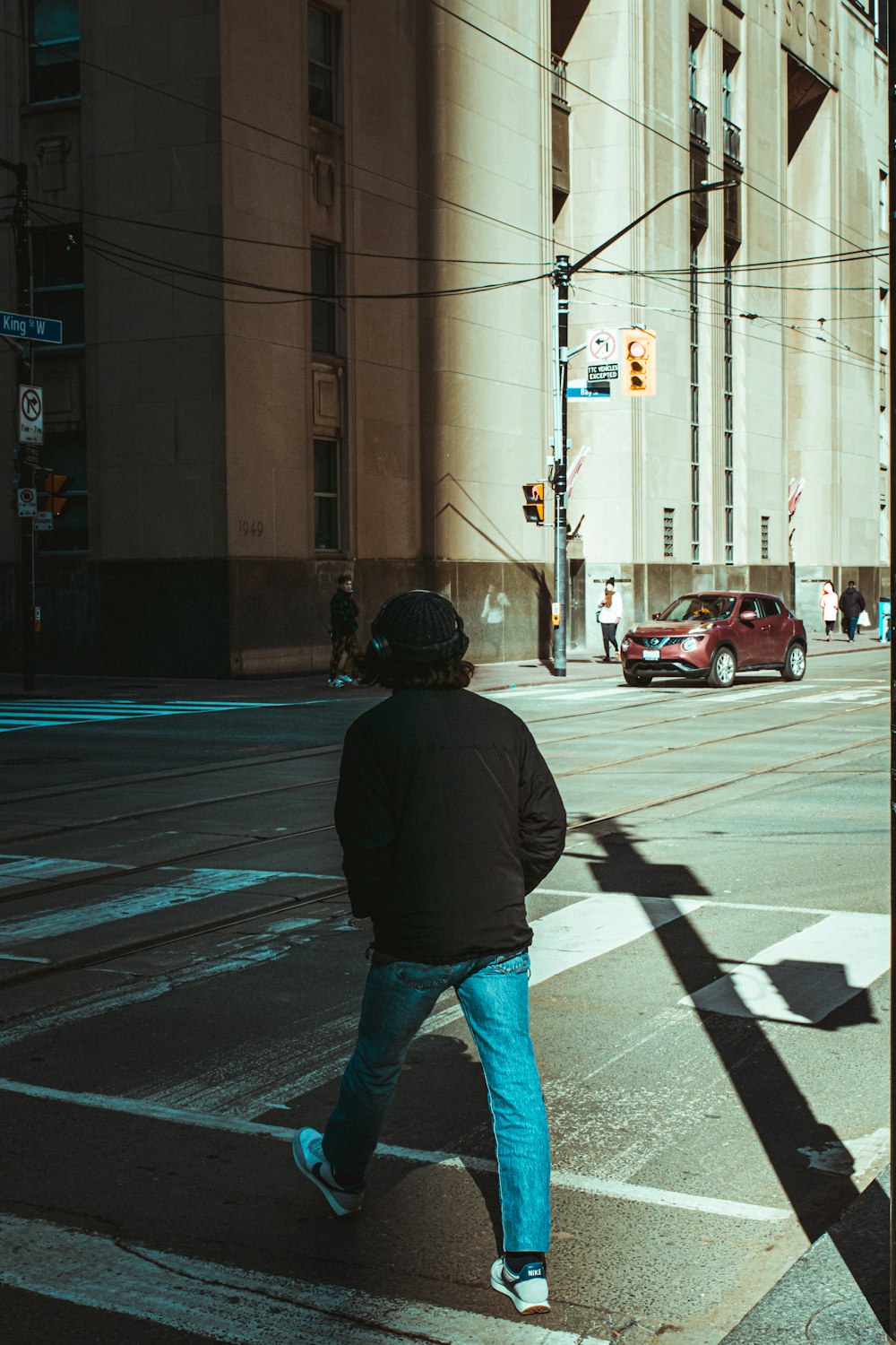 man in black jacket and blue denim jeans standing on pedestrian lane during daytime
