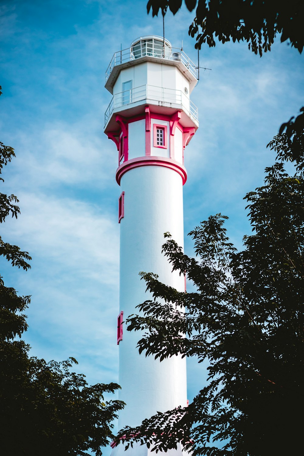 white and red concrete lighthouse near green trees under blue sky during daytime