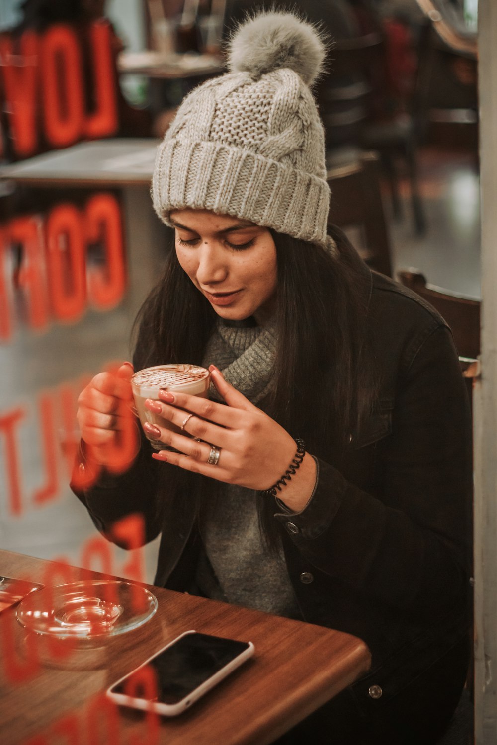 woman in black long sleeve shirt and white knit cap holding clear glass cup