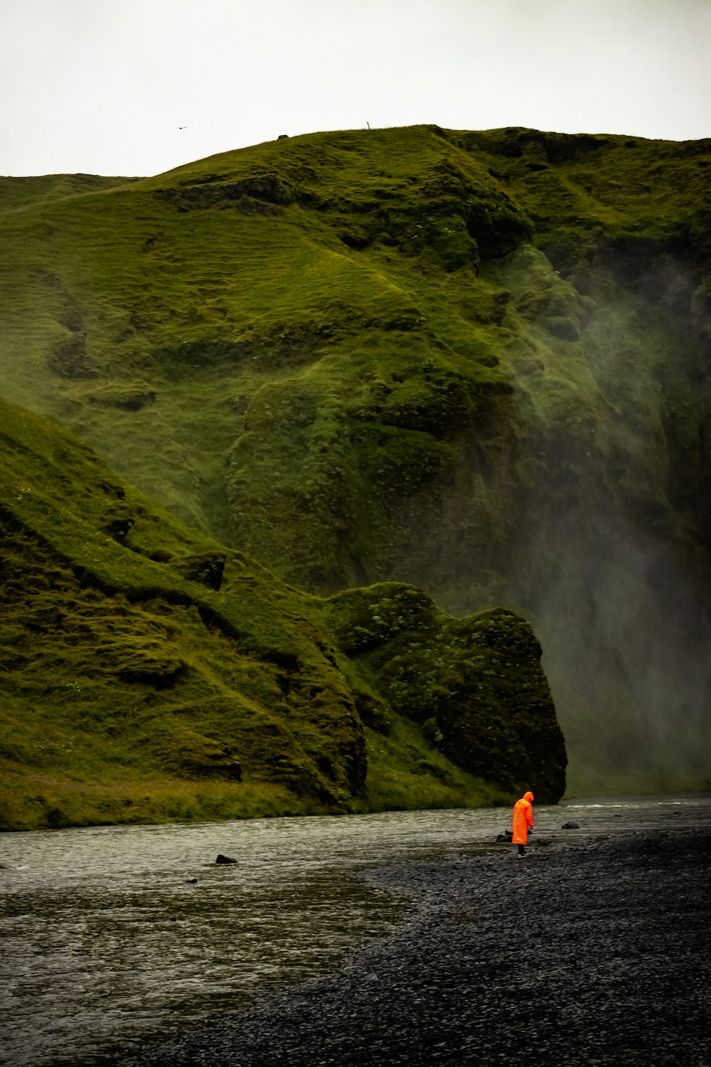 낮 동안 그린 마운틴 근처의 물 위에 서 있는 주황색 재킷을 입은 사람