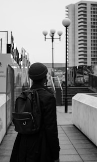 grayscale photo of man in black jacket and knit cap standing near street light