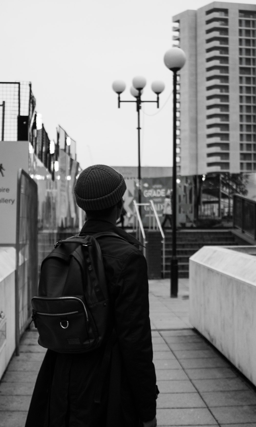 grayscale photo of man in black jacket and knit cap standing near street light