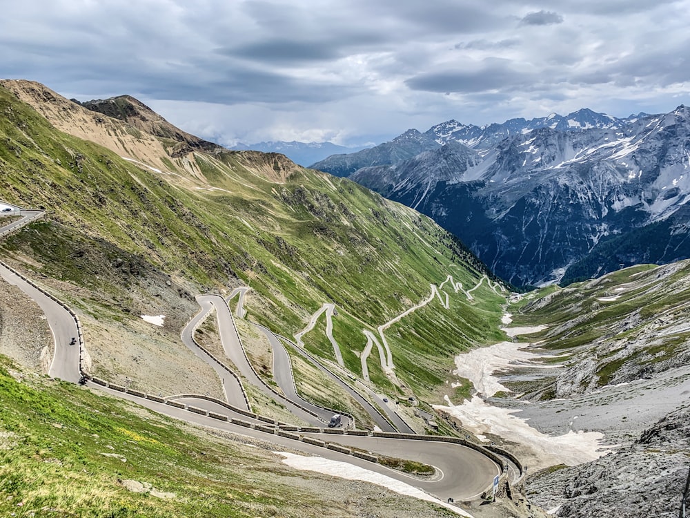 gray asphalt road between green mountains under gray cloudy sky during daytime