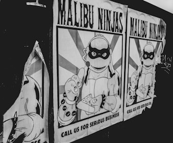A black and white poster featuring a cartoon character resembling a ninja turtle, wearing a ninja mask and holding what appears to be a slice of pizza. The character is muscular and depicted in a retro comic book style. The poster includes text that reads 'Malibu Ninjas' and 'Call us for serious business'. The image shows two similar posters side by side, with one partially torn.
