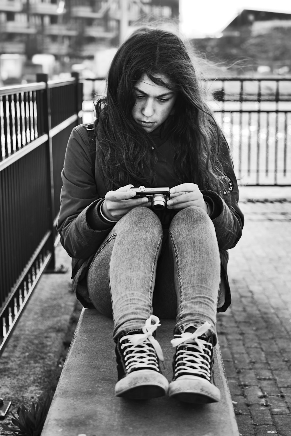 woman in black coat and blue denim jeans sitting on the sidewalk