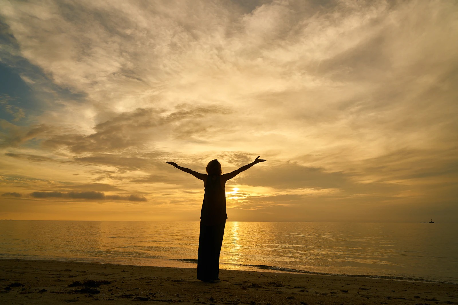 Woman at the beach with arms open at sunset