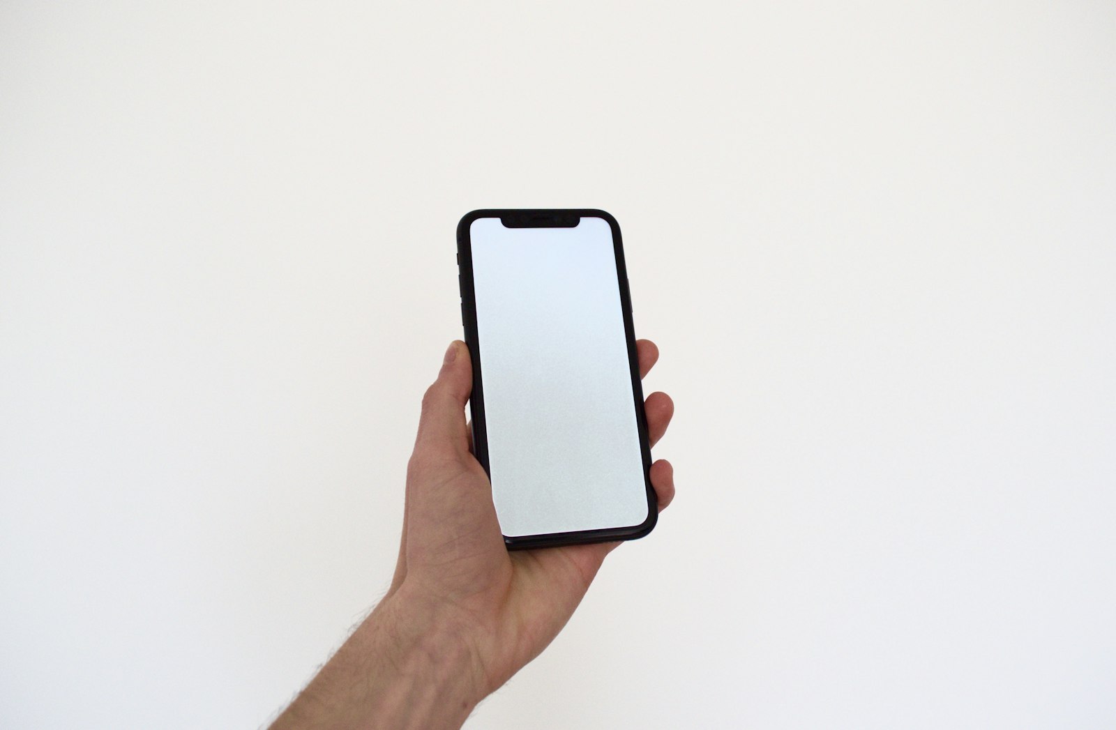 Une main tient un smartphone à l’écran vierge, sur fond blanc