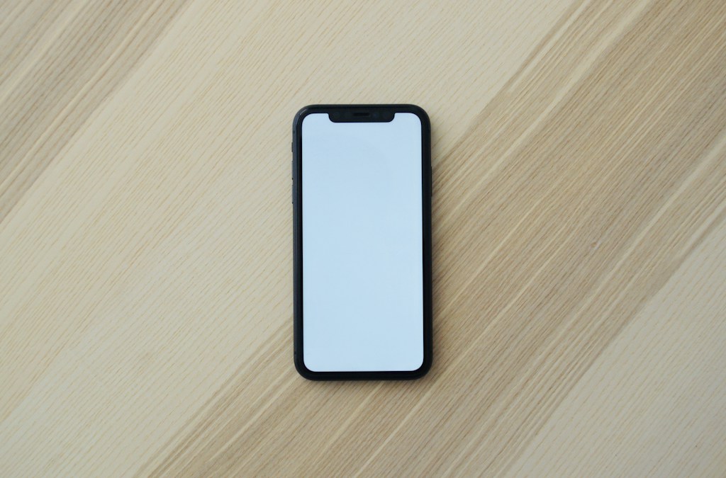 Smartphone noir à écran blanc vu du dessus, posé sur une table en bois clair, en illustration