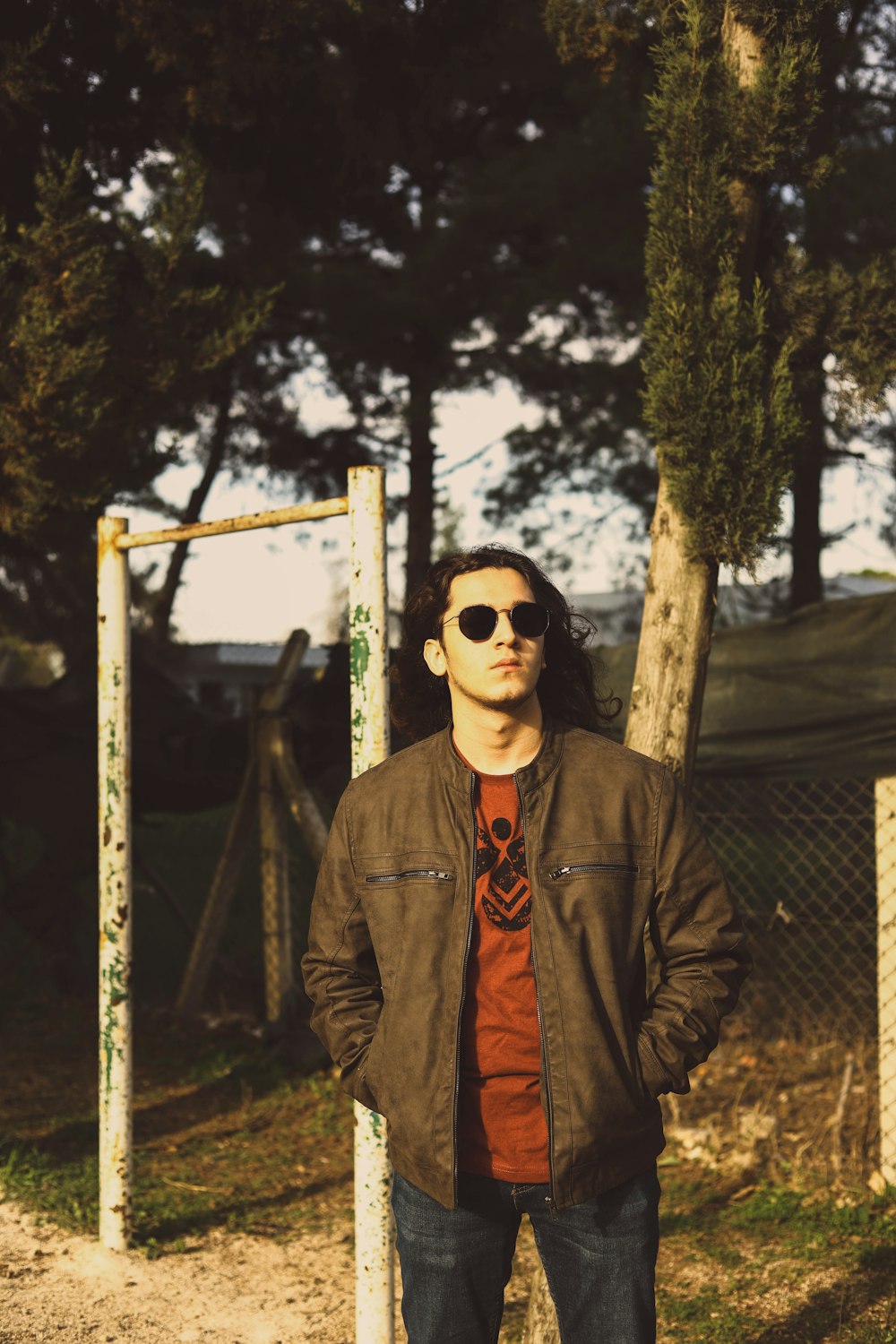 man in black jacket wearing black sunglasses standing near brown wooden fence during daytime