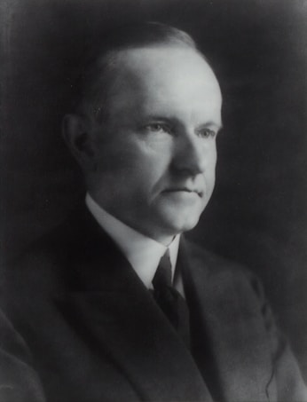 A black and white portrait of a man wearing a suit and tie, facing slightly to the side. The image conveys a sense of formality and seriousness, with soft lighting highlighting the facial features against a dark background.