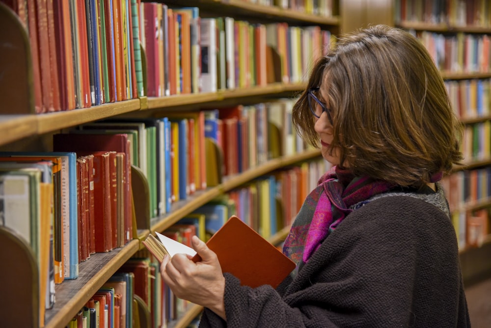 woman in red coat reading book in library