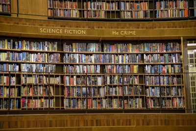 A large wooden bookshelf filled with an extensive collection of books organized into sections labeled as 'Science Fiction' and 'Crime'. The shelves are packed with colorful book spines, featuring diverse titles and authors.
