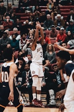 A dynamic basketball game moment featuring players in black and gold uniforms under bright arena lights.