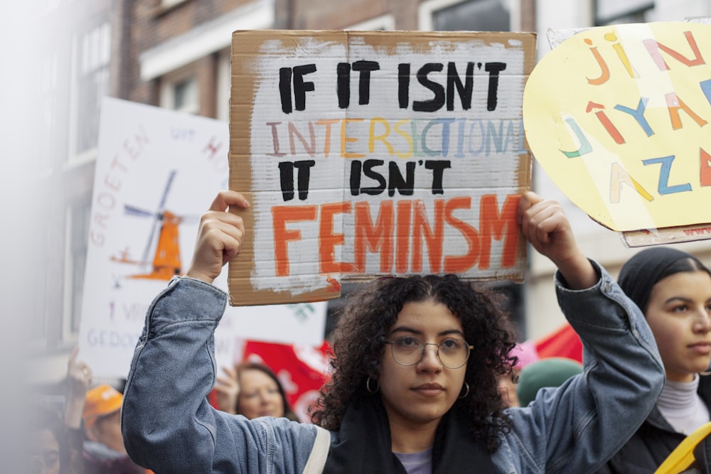 woman in blue denim jacket holding white and red signage