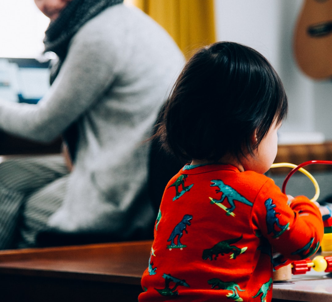 child in red and white floral long sleeve shirt sitting on brown wooden table