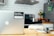 A modern kitchen setting with a silver laptop on a wooden table, featuring a sticker that reads 'Beautiful, free photos.' The background includes a stove with a stainless steel pot, a fruit bowl with various fruits, a tiled backsplash, and a refrigerator with magnets.