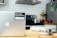 A modern kitchen setting with a silver laptop on a wooden table, featuring a sticker that reads 'Beautiful, free photos.' The background includes a stove with a stainless steel pot, a fruit bowl with various fruits, a tiled backsplash, and a refrigerator with magnets.