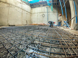 Team of construction workers in hard hats reviewing blueprints on an industrial site.