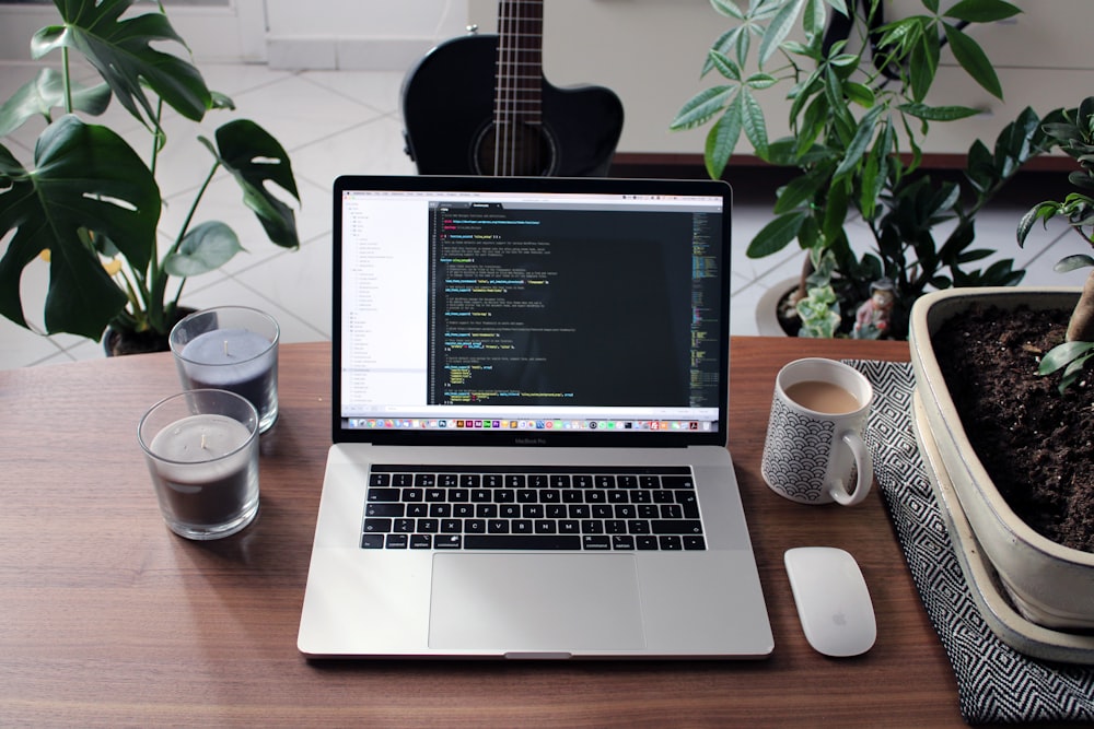 macbook pro ao lado da caneca de cerâmica branca na mesa de madeira marrom