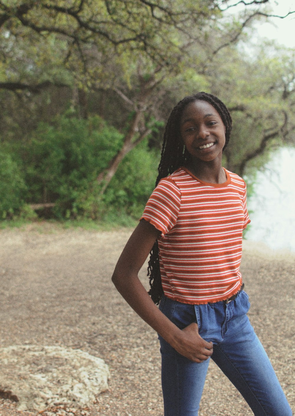 woman in red and white striped shirt and blue denim jeans standing on dirt road during