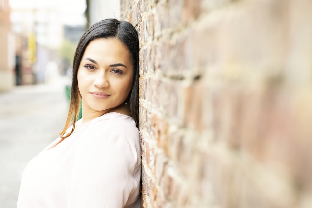 woman in white long sleeve shirt leaning on brown brick wall during daytime