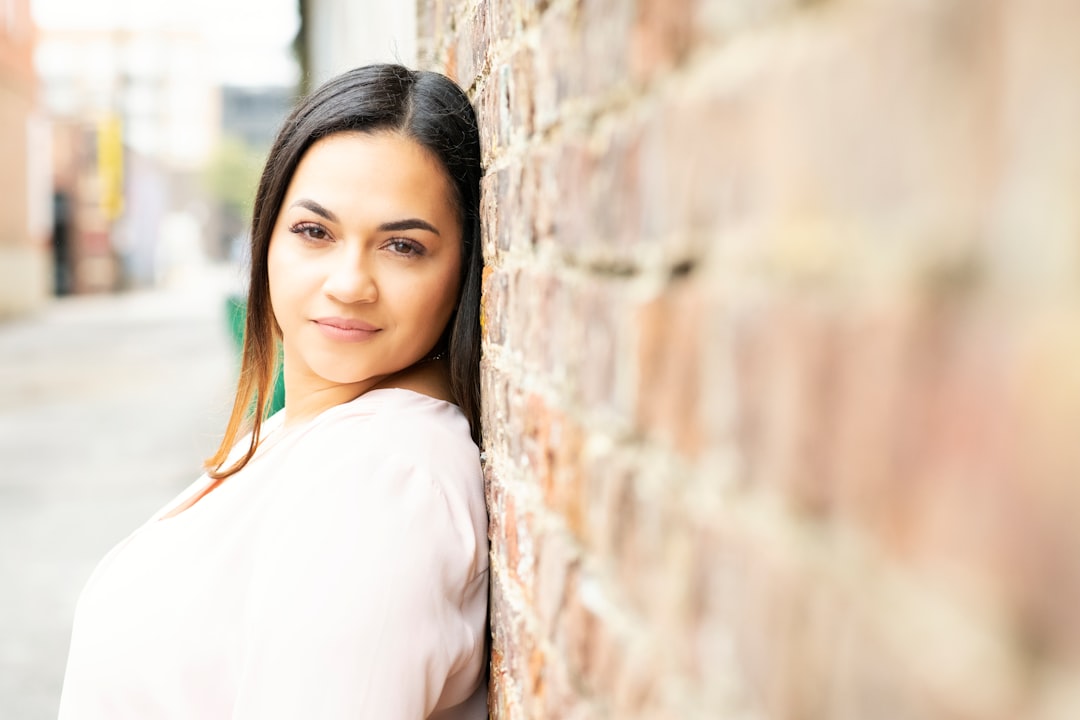 woman in white long sleeve shirt leaning on brown brick wall during daytime