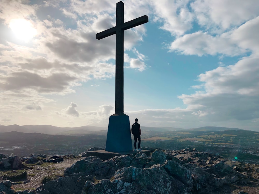 croix noire sur une colline rocheuse sous un ciel nuageux bleu et blanc pendant la journée