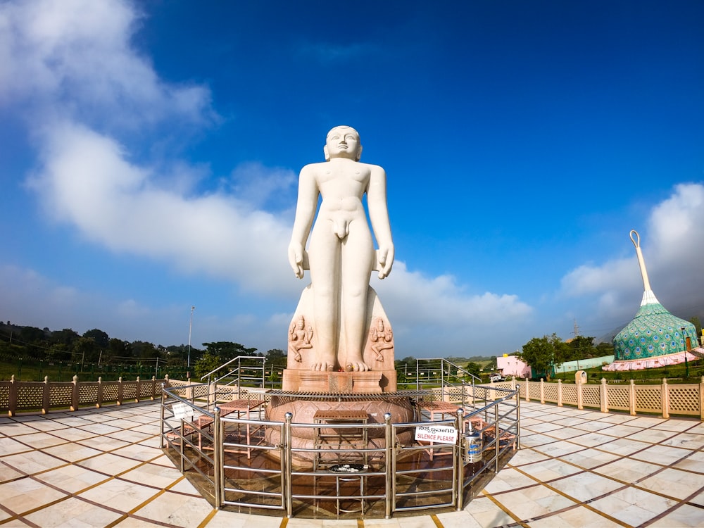 estátua de concreto branco do homem na cerca de metal cinzenta sob o céu azul durante o dia